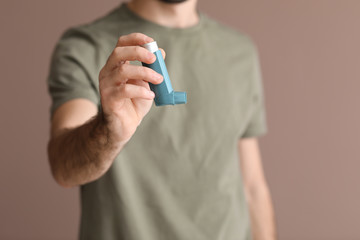 Young man with inhaler on color background, closeup
