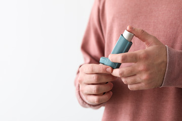 Young man with inhaler on white background, closeup