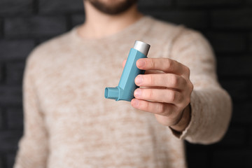 Young man with inhaler on dark background, closeup