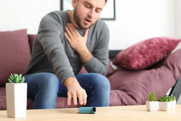 Young man with asthma attack taking inhaler from table