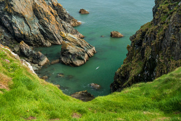 Beautiful landscape on Emerald Isle with green grass and rugged cliffs and a seagull flying above the sea on a summer day, scenic view along Howth Cliff Walk in Dublin, Ireland.