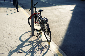Fototapeta na wymiar Sunlit sport bicycle leaned to post by the road