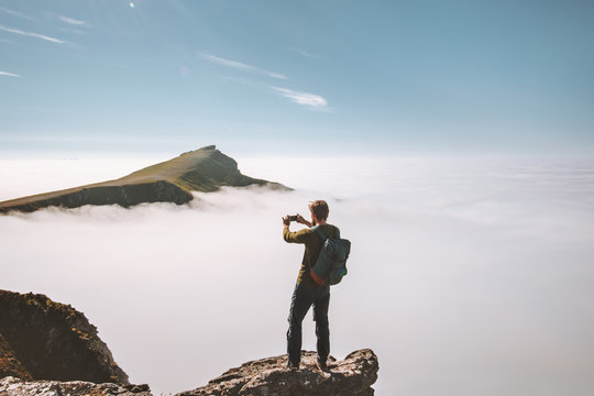 Man traveler taking photo by smartphone in mountains on cliff over clouds Travel blogger vacations lifestyle hobby concept adventure summer trip outdoor