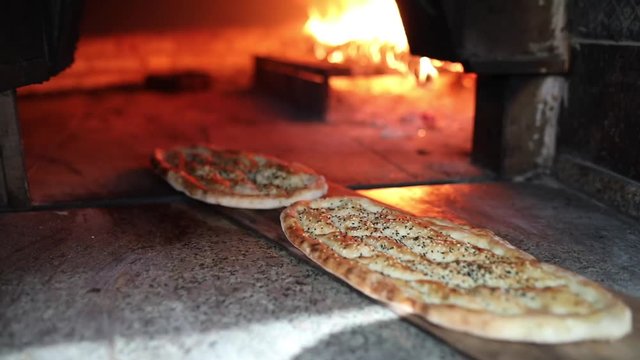 Traditional Turkish Pita or pide bread with sesame on wooden oar in brick oven or stone stove oven. Bakery or bakehouse concept image. Turkish cuisine ramadan iftar product.
