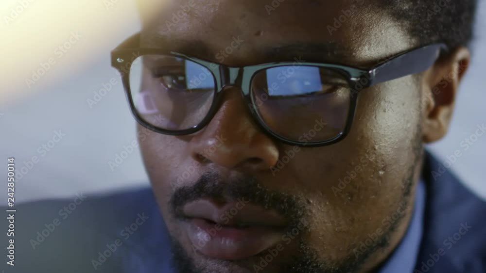 Poster close up face of bearded black businessman in glasses focusing on work while using computer in offic