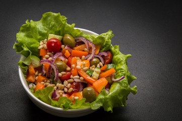 Close up. Vegan, vegetarian food. Bowl of vegetable greek salad with tofu and pine nuts. Black background. Copy space.