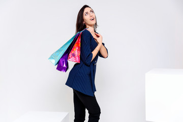 Concept portrait of a girl standing on a white background in a business suit with shopping bags. This is in the middle of the frame, next to the white cubes, next to another cube.