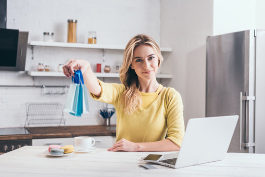 Blonde Woman Holding Small Shopping Bags While Sitting In Kitchen