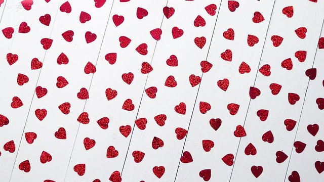Valentine's Day decoration composition. Heart shaped red sequins placed on white wooden table. Romantic background. Flat lay, top view.