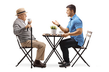 Elderly man and young man sitting at a table having a conversation and drinking coffee