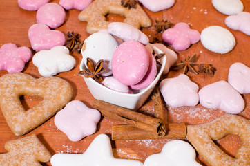 White and pink Christmas gingerbreads in a bowl with a star anise and cinnamon sticks on a wooden kitchen counter