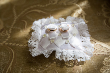 A pair of wedding rings on a white pillow, the edges of which are decorated with lace