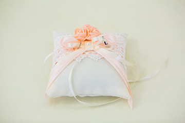 A pair of wedding rings intertwined with a white and pink ribbon on a white pillow.