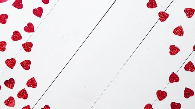 Valentine's Day decoration composition. Heart shaped red sequins placed on white wooden table. Frame with copy space. Romantic background. Flat lay, top view.
