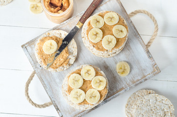 Healthy breakfast with rice cakes with peanut butter and slices of banana on white wooden table....