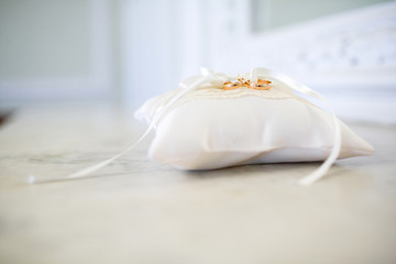 A pair of wedding rings on a white pillow. Rings intertwines white ribbon.