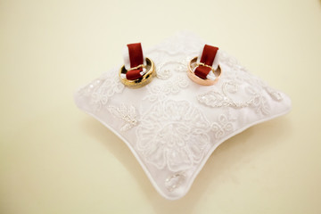 A pair of wedding rings on a white pillow. Rings are fixed on the pillow with a red cloth