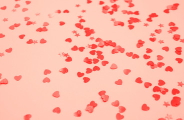 Defocused and blurred beautiful heart and stars shaped red confetti on coral color background.