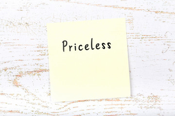 Yellow sticky note on wooden desk with handwritten text priceless
