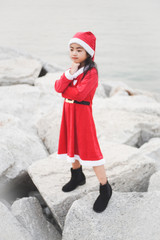 Obraz premium Little Asian girl in Santa Claus dress.Be smiling On the rock dam.
