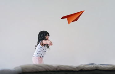 Traveling for Kids or Imagination Concept. Happy and Excited Three Years old Girl Raise Up Hand and Throw a Paper Plane in White Room