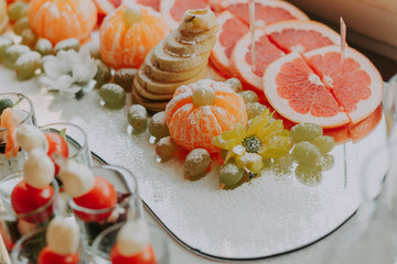 Exquisite cutting of fruit on the holiday table. Bright and colorful tartlets and canapes with oranges, tangerines, grapes and other fruits.