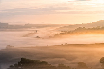 View of village covered in fog during morning sunrise. South moravian landscape with low clouds during a sunrise. Hazy summer scene of small village.