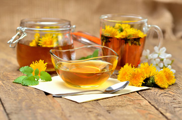 Dandelion honey, herbal tea, full jar of honey, spring flower, fresh mint leaves, spoon and dandelion head around
