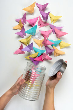 Feminine hands open jar with paper butterflies on white background. Origami