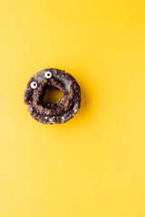 Funny shock face glazed chocolate cake donut on a pastel yellow background, creative minimal Halloween concept with copy space