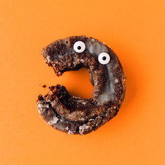 Funny shock face glazed chocolate cake donut on an orange background, creative minimal Halloween concept