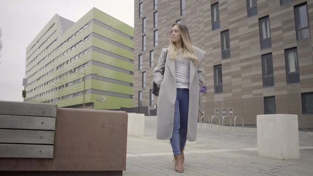 attractive blonde business woman confident grey coat walking city