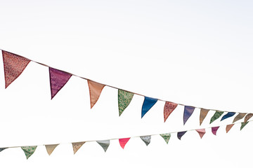Obraz premium Pennants with blue sky background and pale colors hanging on a rope crossing the image during an outdoor event, space for text.