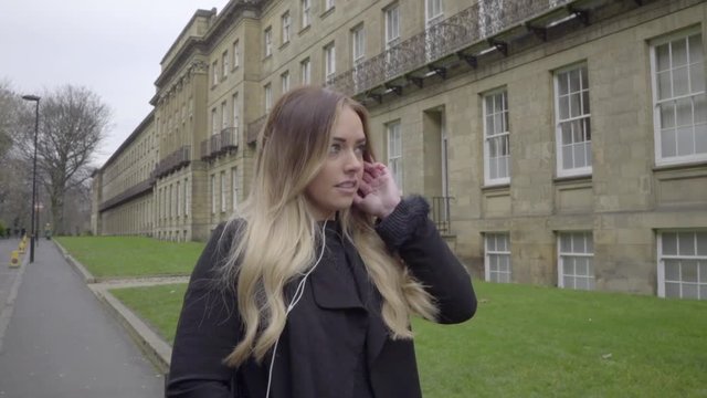 happy woman listening to music on headphones in front of old buildings