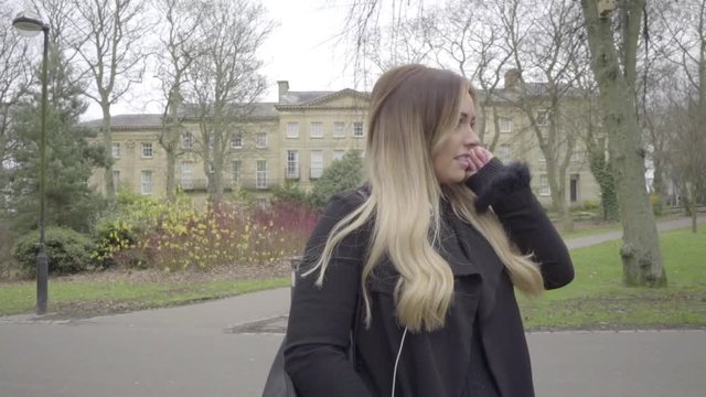 happy woman listening to music on headphones in city park with trees