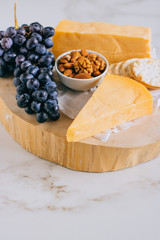 Cheddar cheese, grapes, nuts, honey and cracker in wooden board on marble