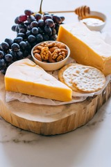 Cheddar cheese, grapes, nuts, honey and cracker in wooden board on marble