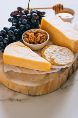 Cheddar cheese, grapes, nuts, honey and cracker in wooden board on marble