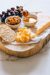 Cheddar cheese, grapes, nuts, honey and cracker in wooden board on marble