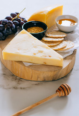 Gruyere cheese, grapes, nuts, honey and cracker in wooden board on marble