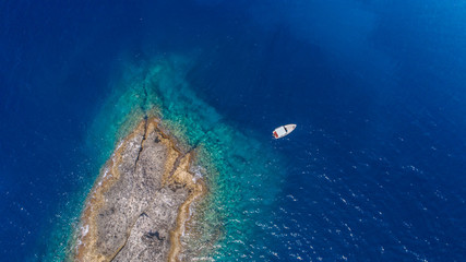 Aerial top view of a deserted island with white boat. Rocky shore of Zannone island near Ponza, Italy. Blue clear water on sunny day.