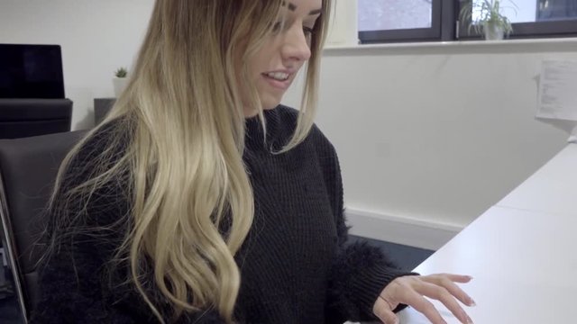 happy attractive blonde woman types email on computer in modern office