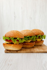 Cheeseburgers on bamboo board on white wooden background, side view.