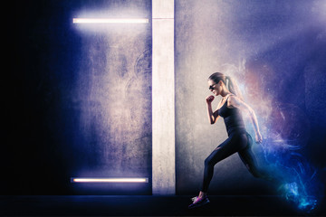 Sporty girl running next to the grungy textured wall with neon lights. Endurance and energy concept.