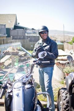 Portrait of a smiling man wearing a helmet and standing next to a motorcycle outside his home.
