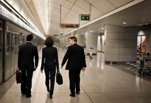 Rear view of businessmen and women walking through a train station.