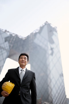 Mid-adult businessman holding a hard hart while standing in a construction site.