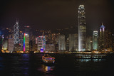 Boat in the harbor in front of illuminated buildings in an urban city at night.