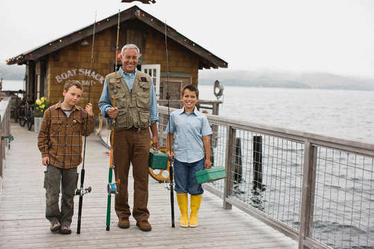 Portrait of a smiling father standing with his two sons on a wharf while holding fishing gear.