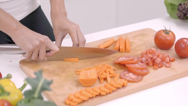 Happy Asian woman cut lots of carrot prepare ingredient for making food in the kitchen, female use organic vegetable for healthy food at home. Lifestyle women making food concept.